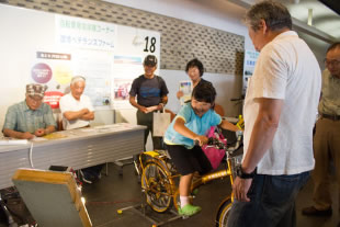 自転車をこいで何ワットの発電できるかな？　「30、40…、やった！すごいね～」環境ベテランズファームの体験コーナー（NPO法人環境ベテランズファーム）