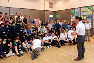 イベントが終了し、来場者が帰っていったあと、出展者を含む関係者全員を前に、簡単な総括をする環境フェスティバル実行委員長の柘植正憲さん。手作り体験広場の机などを撤収して組み上げたホール内の雛壇に参加者が並んで記念撮影を撮るのが恒例になっている。