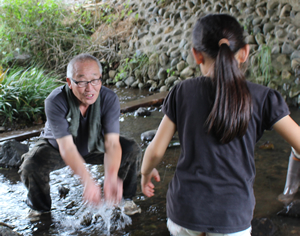 両手で川の水をすくってしぶきを立てる校長の姿が…。