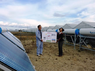新しいハウス横に設置した太陽熱温水器システムの前で看板を寄贈。