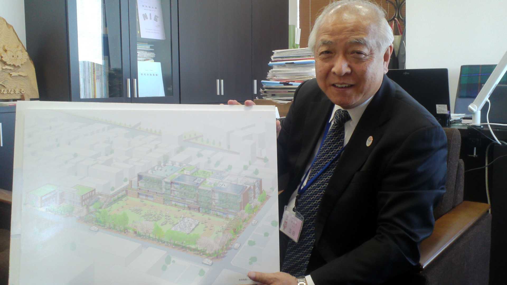 豊島区教育委員会の三田一則教育長。庁舎7階の執務室にて。掲げているのは、区内小学校のエコ改修の計画図面。今年度完成予定を含めて、三田さんの在任8年目で5校の学校改築が完成することになる。