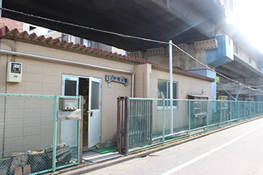 西葛西にあるしぶや木工塾の工房。地下鉄東西線の線路の高架下にある平屋の建物だ。裏には材料の木材が積まれている。