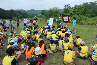 紙芝居をめくって、川遊びの「3つのやくそく」について話をする、山ちゃんこと講師の山崎充哲さん。