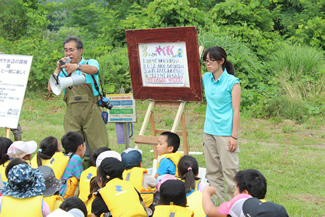紙芝居をめくって、川遊びの「3つのやくそく」について話をする、山ちゃんこと講師の山崎充哲さん。