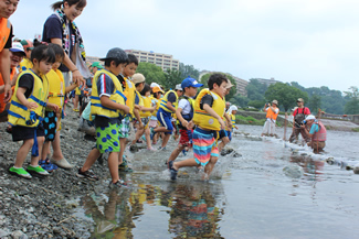 川の中に造った生け簀に入って魚を追いかける子どもたち。手からはみ出す魚を握りしめて、うれしそうな表情を見せる。