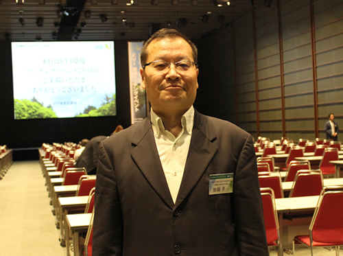 会場をバックにするEVIの加藤孝一さん（カルネコ株式会社代表取締役社長）。