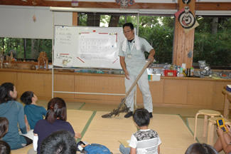 田の草取りに使う「田掻車（たかきぐるま）」を手にする博物館学芸員の佐藤智敬さん。今日の農作業の内容と、作業に関連したお話をしてくださった。