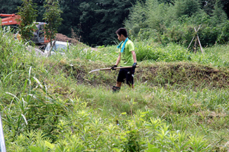 菅生の大沢地区の一角につくられたマウンテンバイクコースで草刈りをする会員の少年。マウンテンバイク歴は7、8年になるという。「今日は小さい子たちが体験に来るので、走りやすいように考えて草を刈っています」と話してくれた。